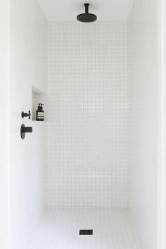 a white tiled shower stall with black fixtures