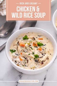 two bowls of chicken and wild rice soup on a marble table with spoons next to it