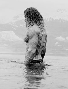 a woman standing in the water with her back to the camera, wearing a wet suit