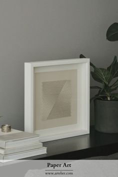 a white frame sitting on top of a table next to a potted plant and two books