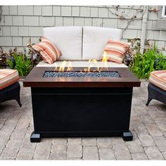 a fire pit sitting next to two chairs on top of a brick patio with pillows