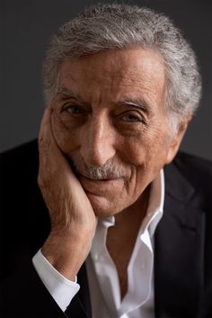 an older man wearing a suit and white shirt with his hand on his chin looking at the camera