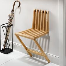 a wooden chair sitting next to an umbrella on top of a stand in front of a white wall