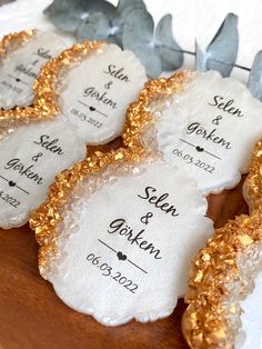 some white and gold wedding favors on a wooden table with silver leaves in the background