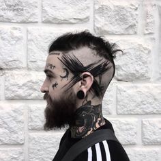 a man with tattoos and piercings on his head standing in front of a brick wall