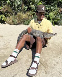 a man sitting in the sand holding an alligator