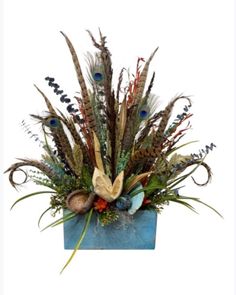 a vase filled with lots of different types of flowers and feathers on top of a blue box