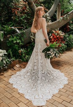 a woman standing in front of a tree wearing a wedding dress with an open back