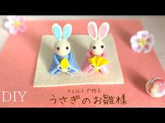 two small plastic rabbits sitting on top of a pink surface with flowers in the background