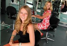 two women sitting at a table in a hair salon, one with long blonde hair