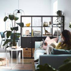 a woman sitting on top of a couch next to a plant in a living room