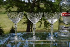 three wine glasses sitting on top of a glass table next to a bottle of alcohol