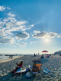 two people sitting in lawn chairs on the beach under a blue sky with clouds above them