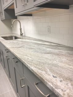 a kitchen with gray cabinets and marble counter tops