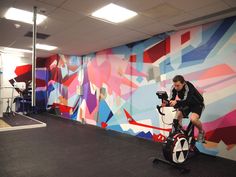 a man riding an exercise bike in front of a colorful wall