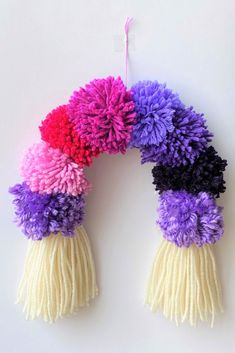 three pom - poms hanging from a string on a white wall, each with different colors