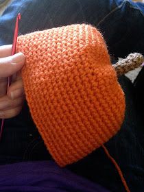 an orange knitted object being held by someone's hand with yarn on it