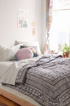 a bed sitting in a bedroom next to a window with lots of pillows on top of it