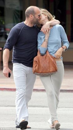 a man and woman kissing while walking down the street with a purse on their back