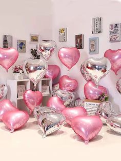 pink and silver heart shaped balloons are arranged on a table in front of a white wall