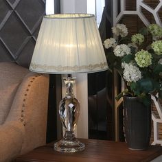 a lamp sitting on top of a wooden table next to a vase filled with flowers