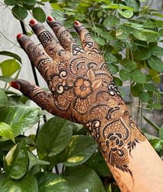 a hand with henna tattoos on it near some plants and leaves in the background