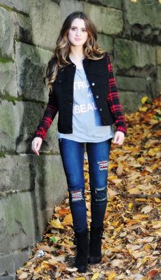 a woman standing in front of a brick wall wearing jeans and jacket with ripped knees