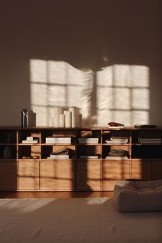 a bed sitting under a window next to a wooden shelf with books on top of it