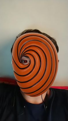 a man wearing an orange and black striped mask with earphones on his head, in front of a white wall