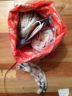 a red bag filled with yarn on top of a wooden floor