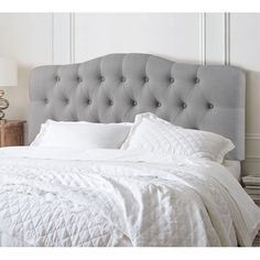 a bed with white sheets and pillows on top of it in a room next to a lamp