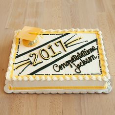 a white and yellow cake with black writing on it sitting on a wooden table next to a knife