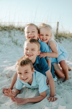 four children are sitting in the sand and one is holding his arm around another child's head