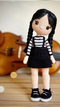 a crocheted doll standing next to a violin on a wooden table with music instruments in the background