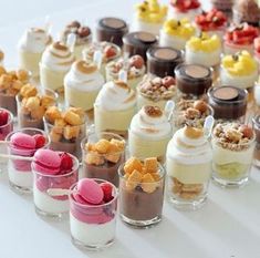 many desserts are lined up in small cups on a white tablecloth with candy and candies