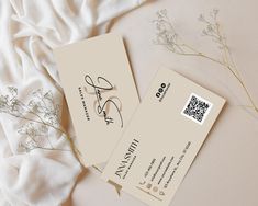 two business cards sitting next to each other on top of a white cloth covered bed