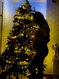 a pregnant woman standing in front of a christmas tree