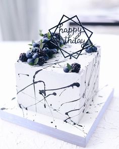 a birthday cake decorated with berries and blackberries on a white tableclothed surface