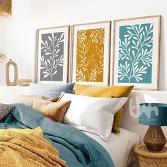 three framed art prints on the wall above a bed with pillows and blankets, next to a lamp