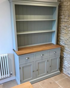 a grey painted china cabinet with wooden top and drawers in a room next to a radiator