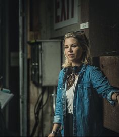 a woman standing next to a wall with her hand on the door and looking at the camera