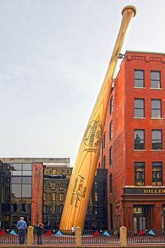 a giant baseball bat in front of a red brick building with people standing around it