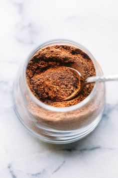 a glass jar filled with brown powder on top of a marble counter next to a spoon