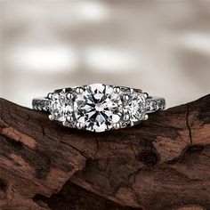 three stone diamond ring sitting on top of a piece of tree bark with white background