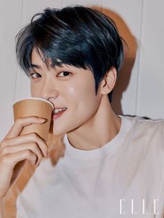 a young man drinking from a cup while wearing a white t - shirt and black hair