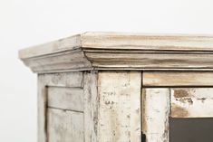 an old white wooden cabinet with glass door and mirror on the top, in front of a plain wall