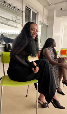 two women sitting on chairs in an office setting, one smiling and the other laughing