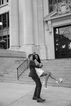 a man and woman kissing on the street in front of an old building with stairs