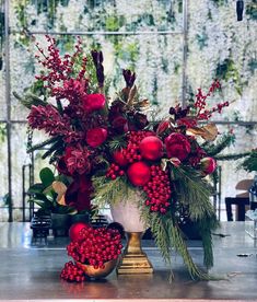 a vase filled with lots of red flowers and greenery on top of a table