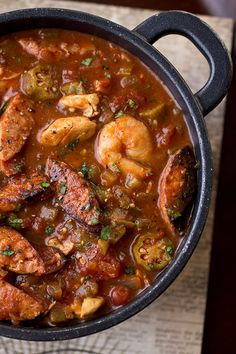 a pot filled with shrimp and vegetables on top of a wooden table next to a napkin